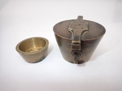 une vieille tasse et une soucoupe en laiton posées sur une surface blanche