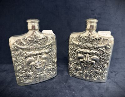 two silver flasks with a face on them on a black background