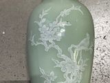 a green vase sitting on a table with a white flower on it