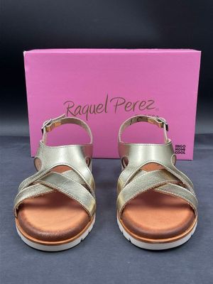 une paire de sandales dorées avec une boîte rose en arrière-plan