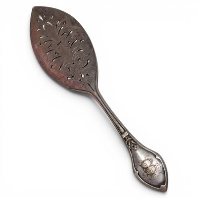 an antique spoon with a leaf design on it on a white surface