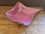 purple glass bowl sitting on top of a wooden table next to a wall