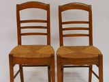 pair of wooden chairs with wicker seats against a white backdrop