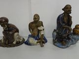 three figurines of people sitting on a white surface, one of them is holding a pot and the other is holding a bowl