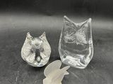 deux figurines en verre représentant des chats assis sur une surface noire