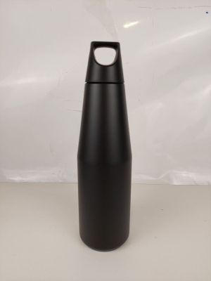 La bouteille d'eau noire est posée sur la table, près du mur blanc.