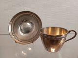 a silver cup and saucer sitting on a glass table