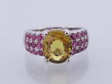 a close up of a ring with a yellow stone surrounded by pink stones