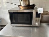 un micro-ondes argenté posé sur un plan de travail, avec une casserole dessus