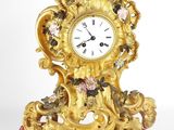 a gold clock sitting on a red cushion on a white surface