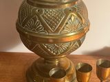 un vase en laiton avec quatre verres et un plateau posés sur une table en bois