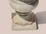 a stone vase on a pedestal with a shadow on the ground