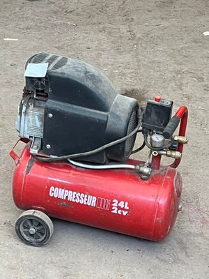 a red compressor sitting on the ground next to a black and white dog
