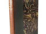 an old book with a gold and black cover sitting on a white surface
