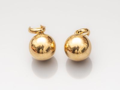 une paire de boucles d'oreilles en forme de boules dorées posées sur une surface blanche