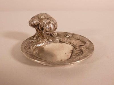 une assiette en argent ornée d'un champignon, posée sur une table blanche