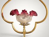 a glass vase with red flowers in it on a gold stand