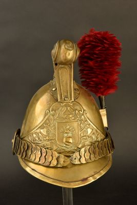 un casque doré orné d'une plume rouge, posé sur un socle