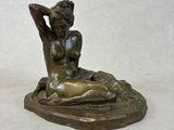 bronze statue of a woman sitting on a rock with her hands behind her head