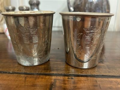 deux tasses en argent posées sur une table en bois, avec un vase en arrière-plan