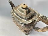 a silver teapot with a handle on a white surface