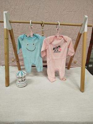 deux vêtements de bébé suspendus à un portant posé sur un lit
