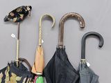 Plusieurs parapluies sont alignés contre un mur gris, avec des étiquettes accrochées dessus.