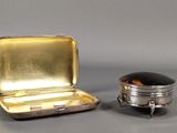 une petite boîte en argent avec un couvercle noir, à côté d'une petite boîte en argent avec un couvercle noir