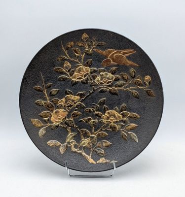 une assiette noire ornée de fleurs et d'oiseaux dorés
