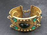 un gros plan d'un bracelet en or orné de pierres vertes
