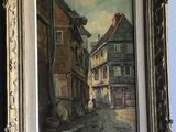 an oil painting of a street scene in a gold frame on a blue carpet