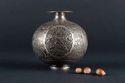 an old silver vase sitting on top of a table next to nuts