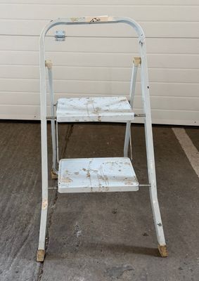 un tabouret en métal blanc devant un mur blanc
