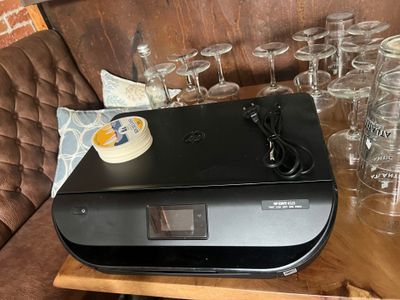 a black printer sitting on top of a wooden table next to glasses