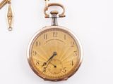 une montre de poche en or avec une chaîne, posée sur une surface blanche