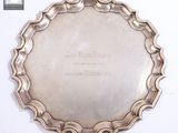 une assiette ancienne en argent, portant une inscription, posée sur une surface blanche