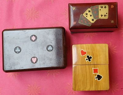 trois boîtes en bois ornées de cartes à jouer, posées sur un fond rose