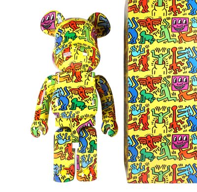 un ours jaune orné d'un motif graffiti coloré, à côté d'une boîte contenant un ours en peluche