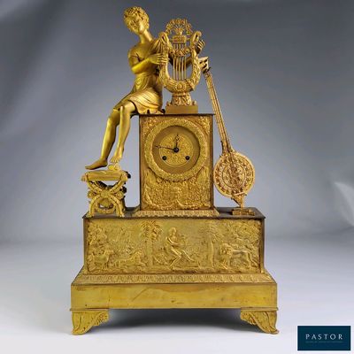 a gold clock with a woman sitting on top of it