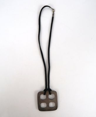 un collier composé d'un bloc de bois suspendu à un cordon, posé sur une surface blanche