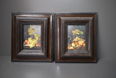 une paire de tableaux encadrés représentant des fruits et des fleurs posés sur une table
