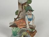 a figurine of a boy sitting on a tree stump with a duck and ducklings