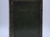 an old book with a black cover sitting on top of a white surface