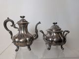 two silver teapots sitting on a glass table