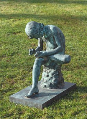 une statue représentant un homme assis sur un rocher dans l'herbe