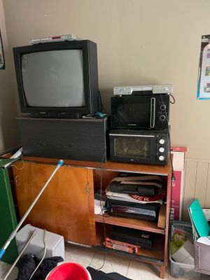 une télévision et un micro-ondes dans une pièce où le sol est encombré d'objets
