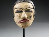 une image représentant un masque en bois posé sur un socle, sur fond noir