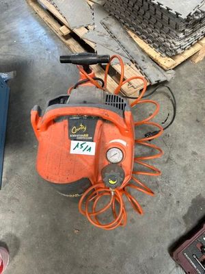 un compresseur d'air orange et noir posé sur le sol, à côté d'une pile de cartons