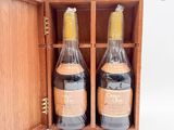 deux bouteilles de vin se trouvent dans une caisse en bois posée sur une surface blanche