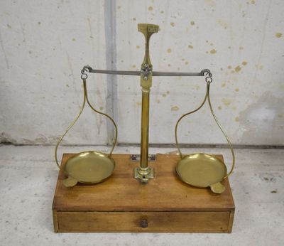 une vieille balance en laiton avec un socle en bois sur lequel reposent deux plateaux en laiton